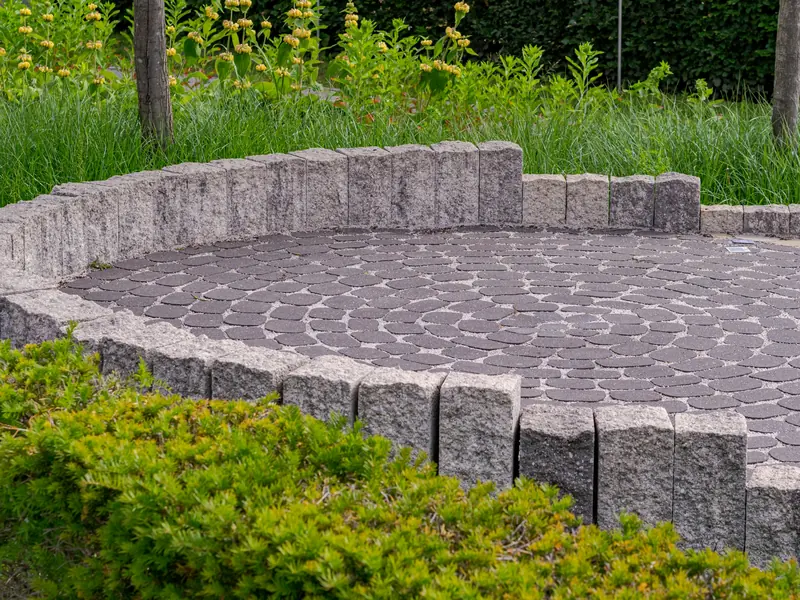 Terrasse ronde pavée, bordée de pierres et entourée de végétation